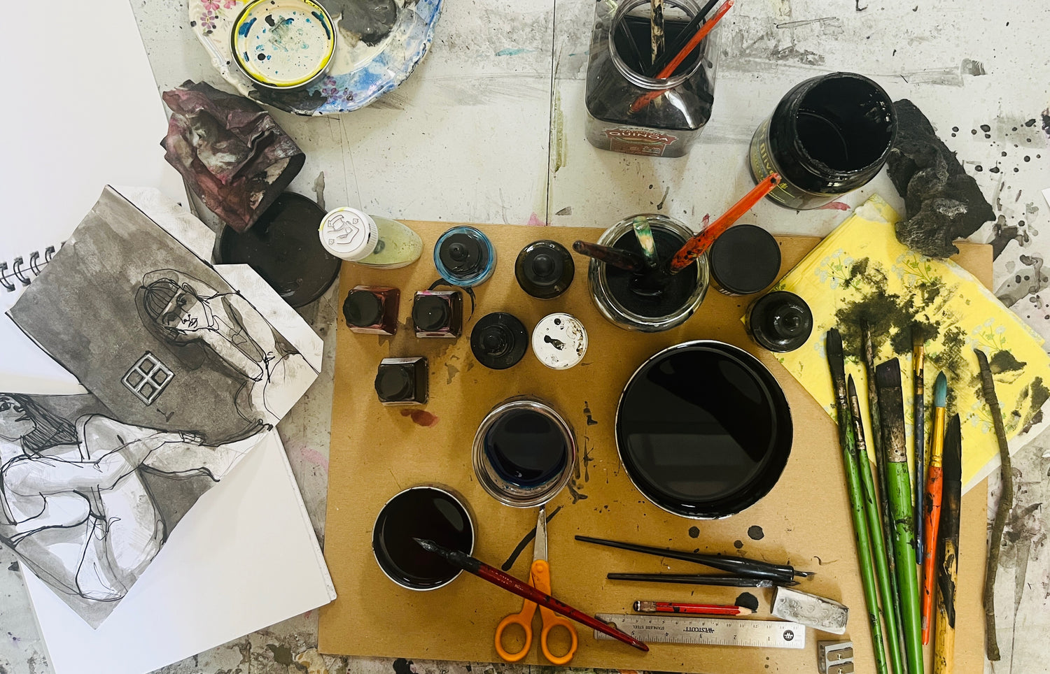 Art supplies including ink bottles, brushes, and a drawing on a table.