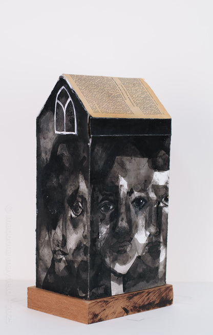 house sculpture with many faces on the walls and a book page on the roof